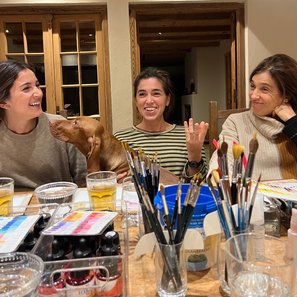 Taller a domicilio: tres amigas se ríen alrededor de la mesa, con un perro que se suma.