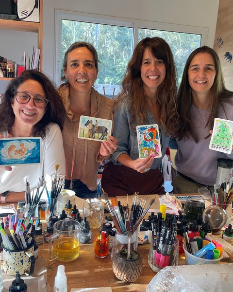 Cuatro amigas muestran sus postales terminadas alrededor de la mesa del taller.